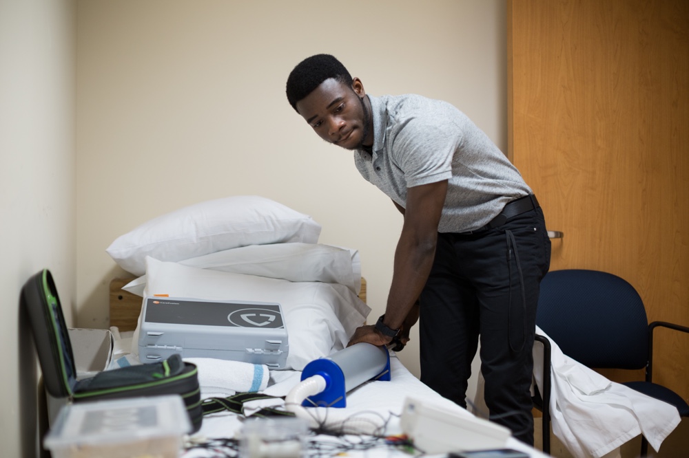 Ryerson alumnus Joseph Makanjuola arranges equipment on a bed in the Toronto Rehabilitation Institute’s sleep clinic.